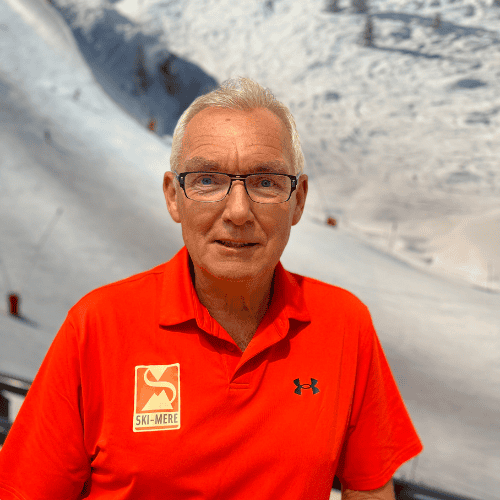 Man in rood sportshirt met Ski-Mere logo voor een achtergrond van een indoor skibaan.