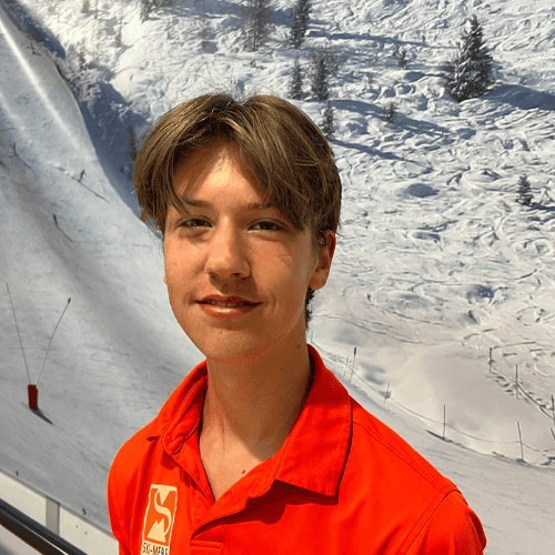 Mannelijke ski-instructeur in rood jack op besneeuwd skigebied tijdens winter, glimlacht naar camera.