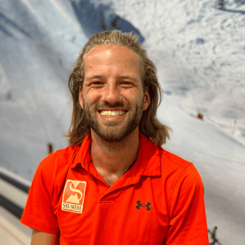 Korte omschrijving van de alt-tekst: Geduldige instructeur in een rode ski-outfit met ski- en snowboardlessen in een indoor skipiste in Almere.