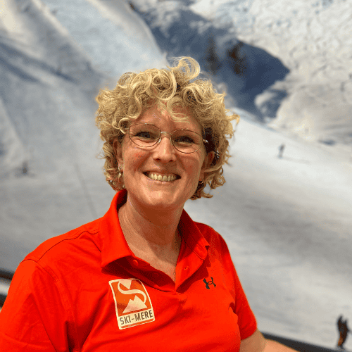 Alt: Vrouw met krullend haar en een rode ski- of snowboardoutfit op indoor rolpiste in Almere.