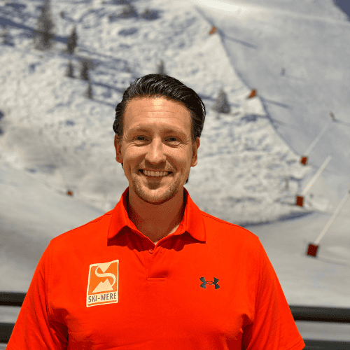 Ski-Meer instructeur in rode sportoutfit met indoor ski- of snowboardbaan op de achtergrond.