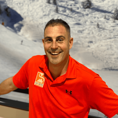Man in rode ski- of snowboardoutfit met indoor ski-achtergrond, promotend lessen en activiteiten bij Ski-Mere in Almere.