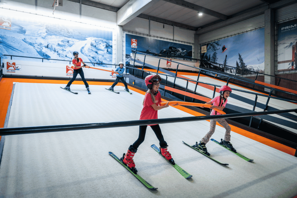 Ski-mere indoor ski- en snowboardrolpiste met kinderen die lessen volgen en plezier maken.
