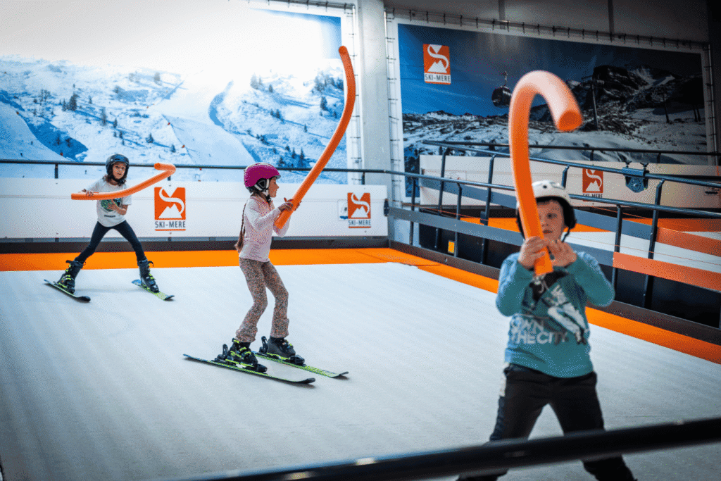 Scholieren leren skiën op de indoor skibaan in Almere met behulp van foam-pakken en gepaste lessen.