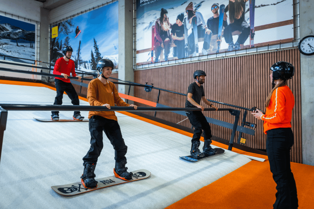 Snelle, jonge skiërs op de indoor rolpiste in Almere met instructeur die tips geeft.